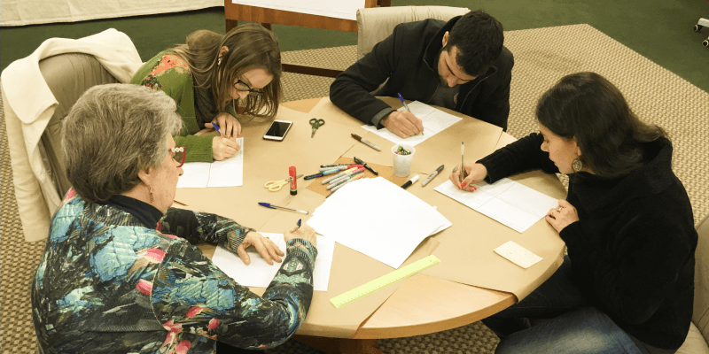 Uma mesa rodeada por 4 pessoas sentadas fazendo uma atividade em um workshop de cocriação com usuários para o projeto de Zaffari.